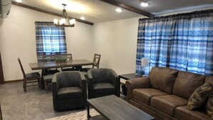 A living room with a brown leather sofa, two armchairs, a coffee table, and a dining area with a table and chairs.