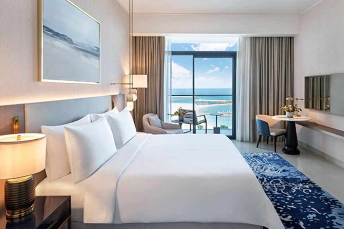 A hotel room with a large bed, a desk, a chair, a TV, and a view of the ocean.