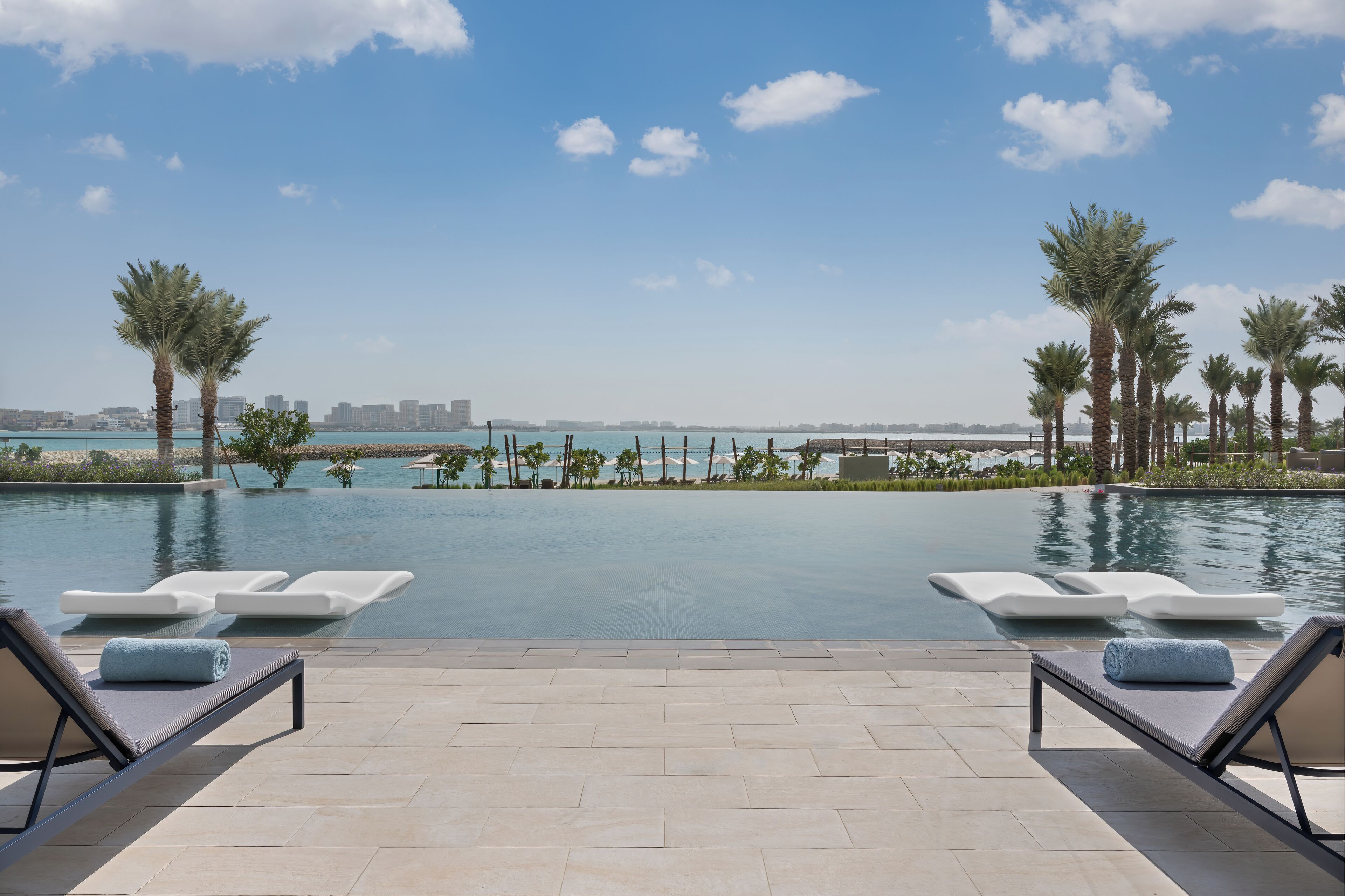 Zona de piscina con sillones de descanso y vistas al mar y al horizonte de la ciudad.