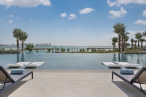 A poolside area with lounge chairs and a view of the sea and city skyline.