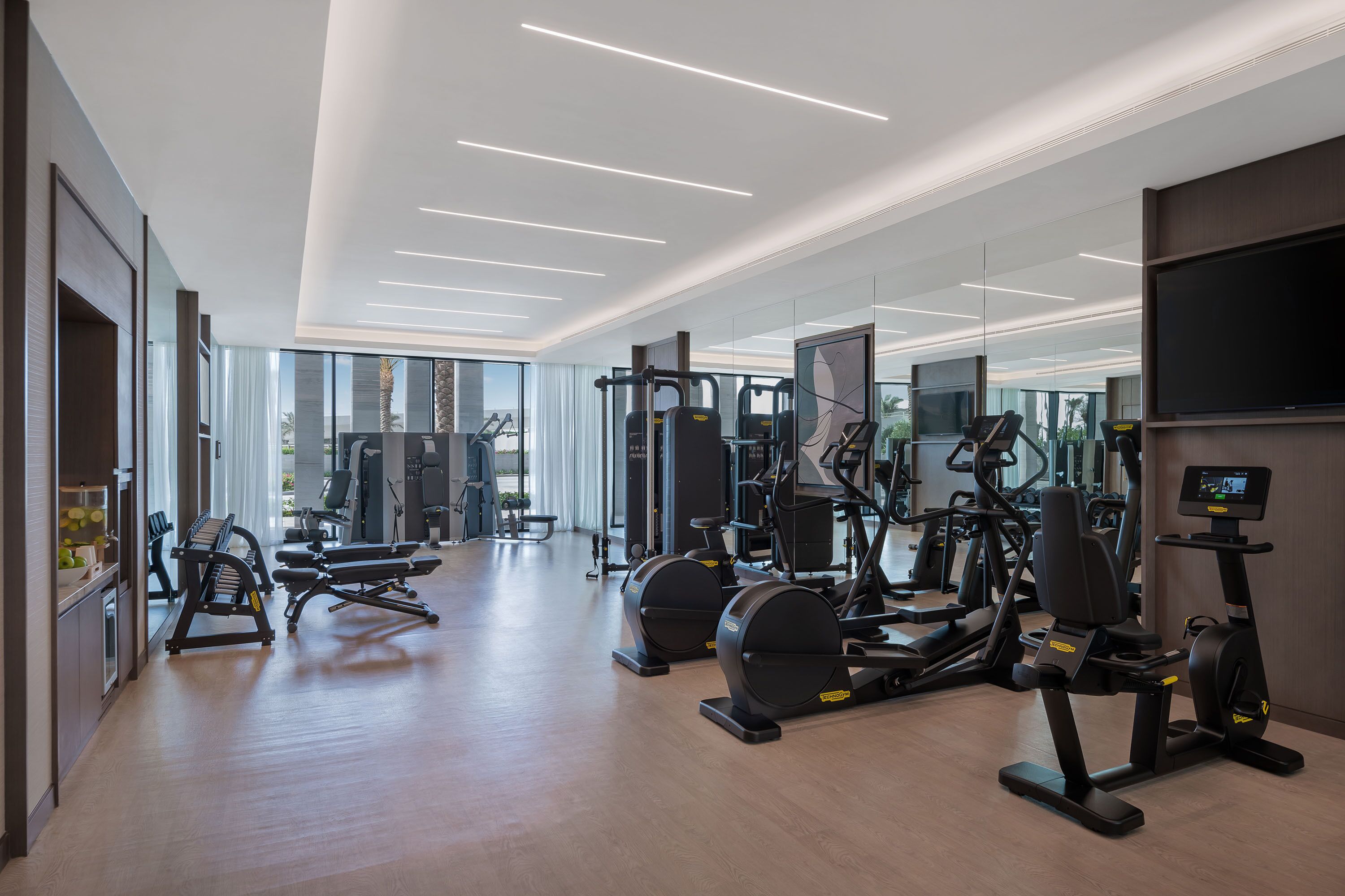 Un gimnasio moderno con diverso equipo de ejercicio, amplias ventanas y una televisión de pantalla plana.