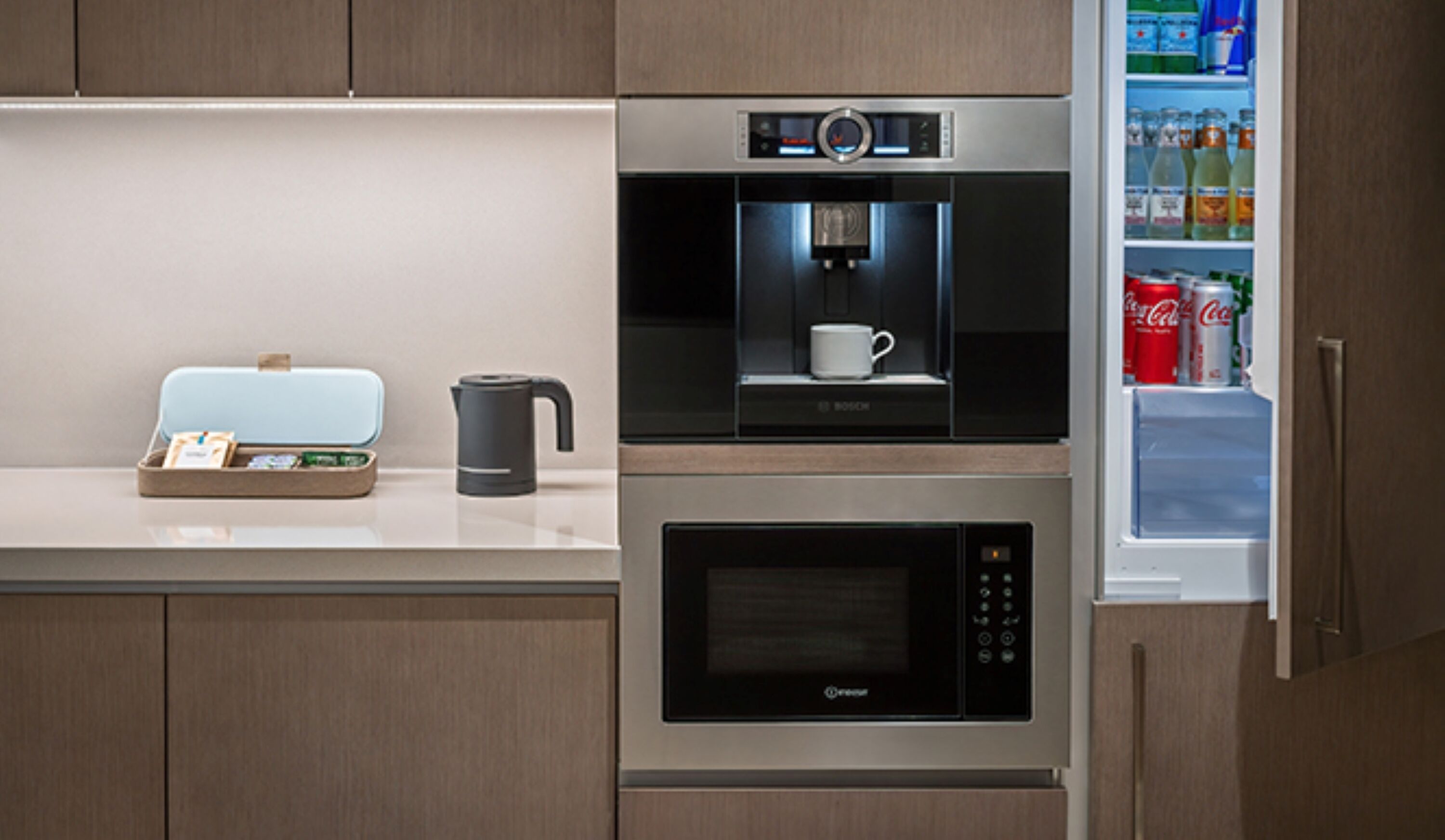 Una cocina equipada con cafetera, microondas y refrigerador lleno de bebidas.
