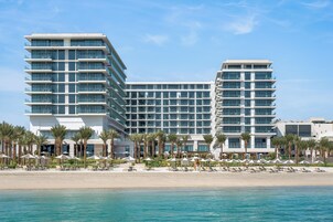 A modern hotel with multiple floors, a beachfront location, and a pool area with umbrellas.
