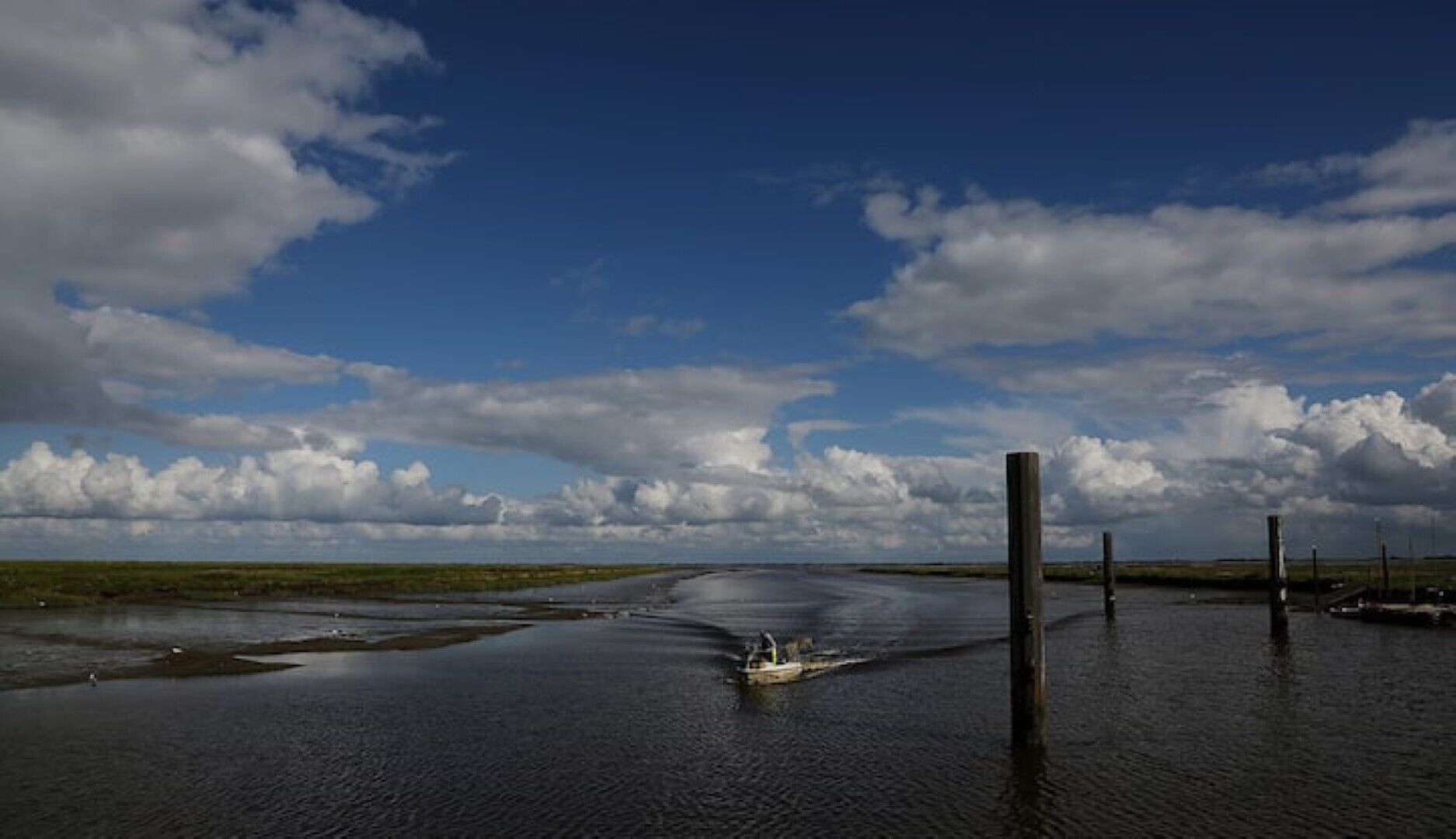 A river with a small boat and wooden posts in the water.