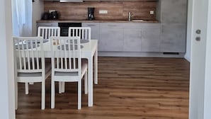 Kompakti keittiö, jossa on harmaat kaapit, puinen työtaso ja ruokailutila valkoisilla tuoleilla.