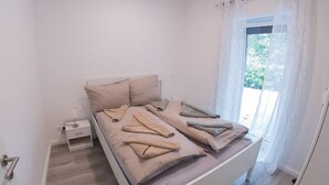 A minimalist bedroom with a bed, a nightstand, and a window with curtains. - "backbord"- Moderne Ferienwohnung in Varel (Varel)