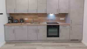 A compact kitchen with grey cabinets, a wooden countertop, a built-in oven, and a coffee maker. - "backbord"- Moderne Ferienwohnung in Varel (Varel)