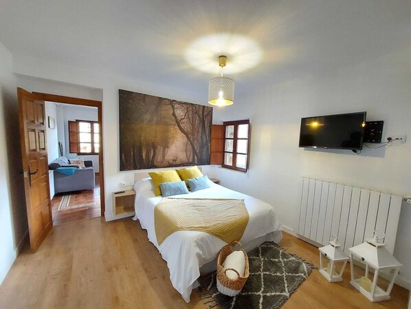 Un dormitorio con cama, televisor, un cuadro y vista a otra habitación.