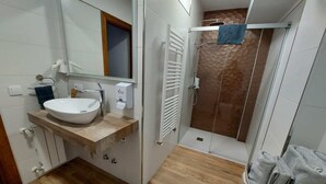 A bathroom with a white sink, a mirror, a towel rack, a shower with a glass door, and a wooden floor.