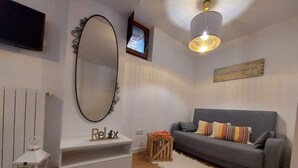 A living room with a grey sofa, a white console table with 'Relax' decor, a large mirror, a small table with a bowl, and a hanging light fixture.