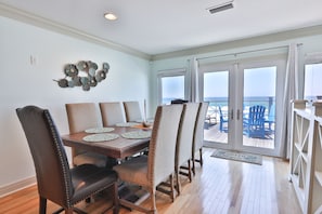 A dining area with a wooden table and chairs, a decorative wall piece, and a view of the ocean through large glass doors.