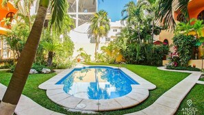 A swimming pool surrounded by palm trees and a well-maintained lawn, with a building in the background. - Rooftop Terrace and Pool Near Mamitas Beach (Playa del Carmen)