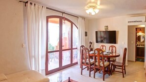 A living room with a sofa, dining table with chairs, a TV, and a sliding glass door to the outside. - Rooftop Terrace and Pool Near Mamitas Beach (Playa del Carmen)