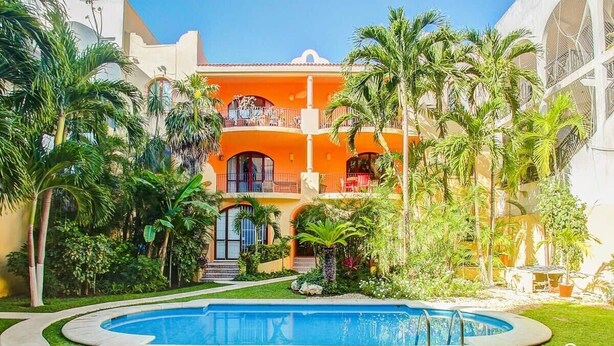 A multi-story building with a pool surrounded by palm trees and a well-maintained lawn. - Rooftop Terrace and Pool Near Mamitas Beach (Playa del Carmen)