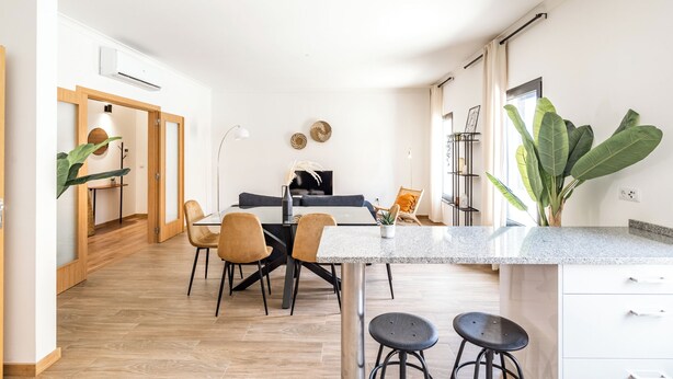 Cozinha moderna com bancada de granito, dois banquetas de bar e uma área de refeições com mesa e cadeiras.