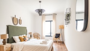 Quarto com cama, mesas de cabeceira, uma cadeira, abajur e espelho.