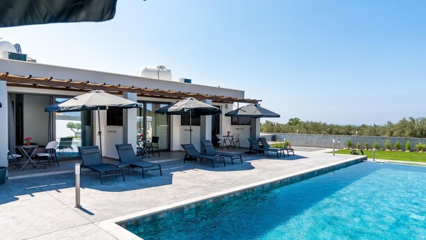 Area piscina moderna all'aperto con lettini e ombrelloni, una piscina blu cristallina e vista sul paesaggio.