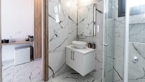Un bagno moderno con rivestimento in marmo, un lavandino bianco e un box doccia in vetro.