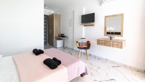 A modern hotel room with a bed, a desk, a chair, a TV, a mirror, and an air conditioning unit.