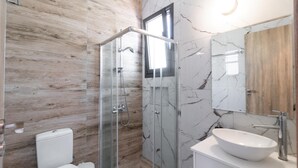 A modern bathroom with a glass-enclosed shower, a white toilet, and a marble-tiled vanity with a large sink.