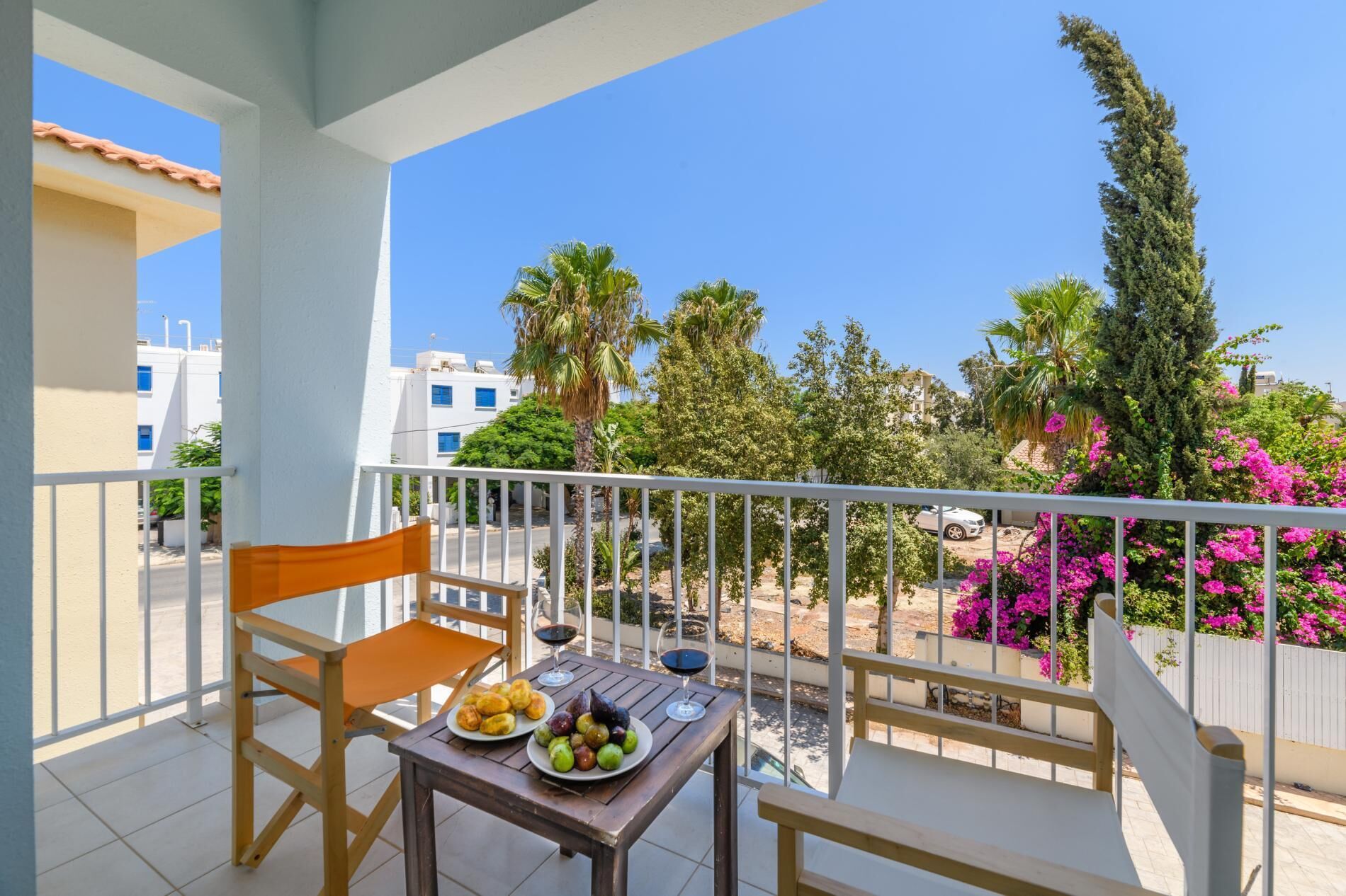 A balcony with a table set for two, featuring a plate of fruit and a glass of red wine.