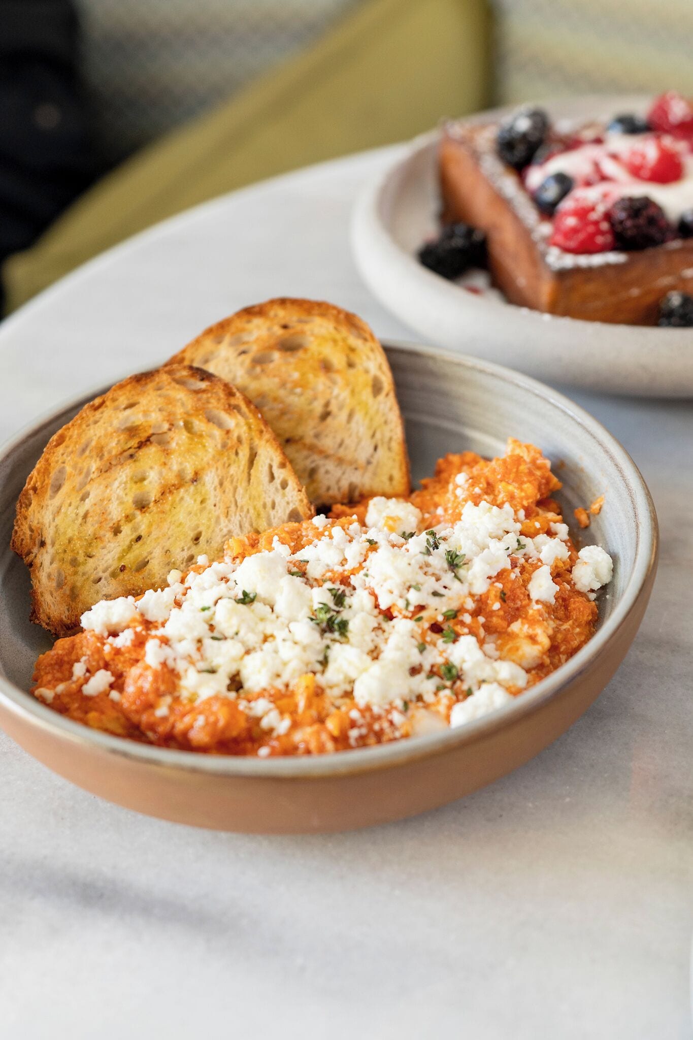 A bowl of food with bread and a plate of berries in the background.