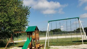 Un’area giochi con una casetta di legno, uno scivolo verde e altalene.