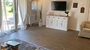 Een moderne woonkamer met een bank, een glazen salontafel en een flatscreen televisie aan de muur.