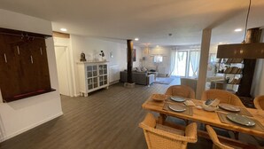 Een ruime woonkamer met een eettafel voor vier personen, een bank en een houten kast.