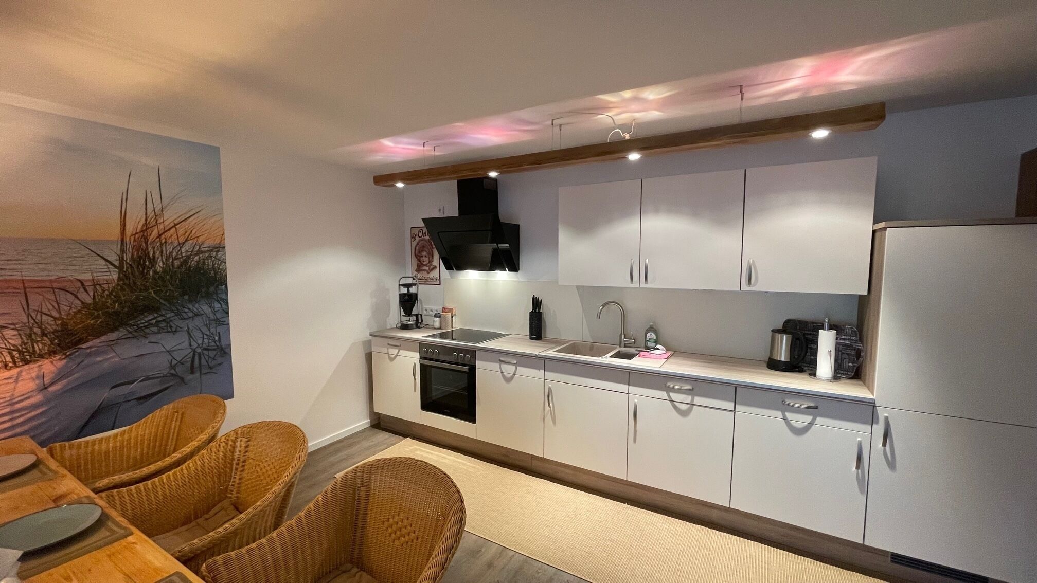 A modern kitchen with white cabinets, a black range hood, and a dining area with wicker chairs.