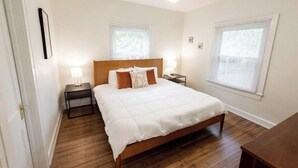 Un dormitorio con una cama de madera, dos mesitas de noche con lámparas y dos ventanas con persianas.
