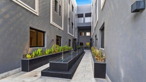 Un patio moderno con suelo de baldosas, macetas negras con plantas verdes y cielo despejado.