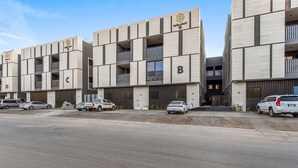 Un edificio moderno con varios balcones y un estacionamiento con varios coches.