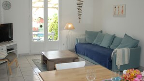 A living room with a television, a sofa, a coffee table, and a dining table. - Maison Individuelle Avec Jardin (Angles)