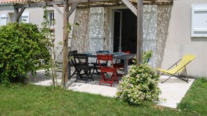 A patio with a table and chairs, a yellow lounge chair, and a small garden area. - Maison Individuelle Avec Jardin (Angles)