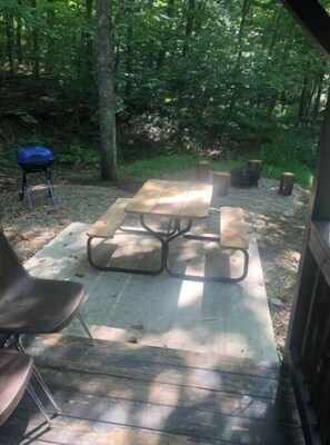 Relax in a serene wooded setting with a picnic table and benches on a spacious outdoor deck.