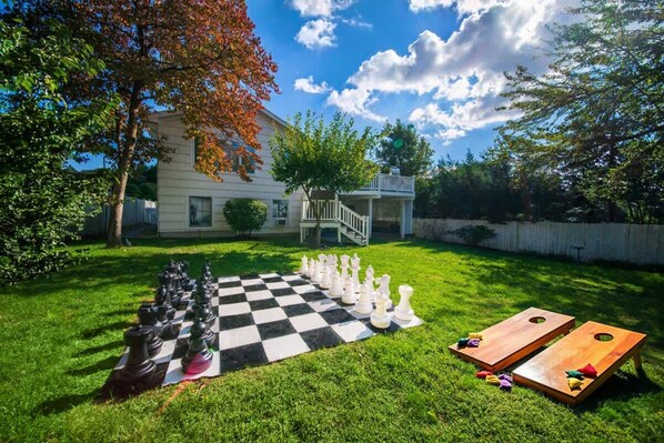 A backyard with a checkered game board, chess pieces, and two wooden tables.