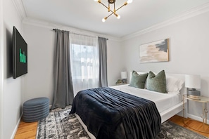 A modern bedroom with a bed, curtains, a mounted TV, a bedside table, and a painting on the wall. - New Beach Home near Stamford Downtown/Shippan (Stamford)