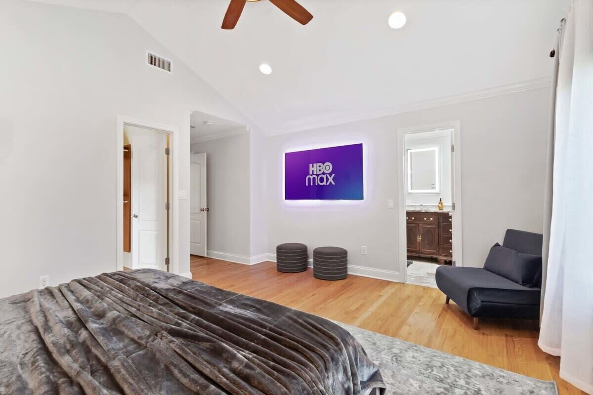 Een moderne slaapkamer met een bed, een bank, een televisie waarop HBO Max wordt getoond, en een houten vloer.