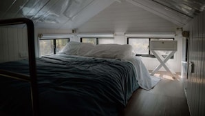 Una cama individual en una habitación con techo inclinado, ventana y una mesita.