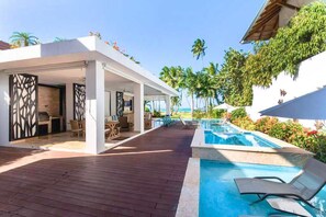 Un espace piscine aménagé dans un complexe hôtelier, avec une terrasse en bois, des chaises longues et une vue sur l’océan.
