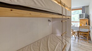 A bunk bed with a wooden frame and a white mattress. There is a table with chairs and a television in the room. - Soyouz-Vanguard 10 - Studio Apartment, Sleeps 4 (Villarembert)