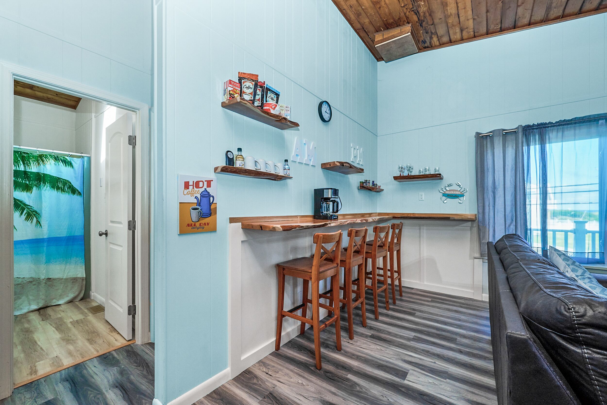 Un espacio habitable compacto con zona de cocina, taburetes de madera, una cafetera y un reloj en la pared.