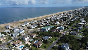 Vue aérienne d’une zone résidentielle côtière, avec des maisons, une plage et un ciel dégagé.
