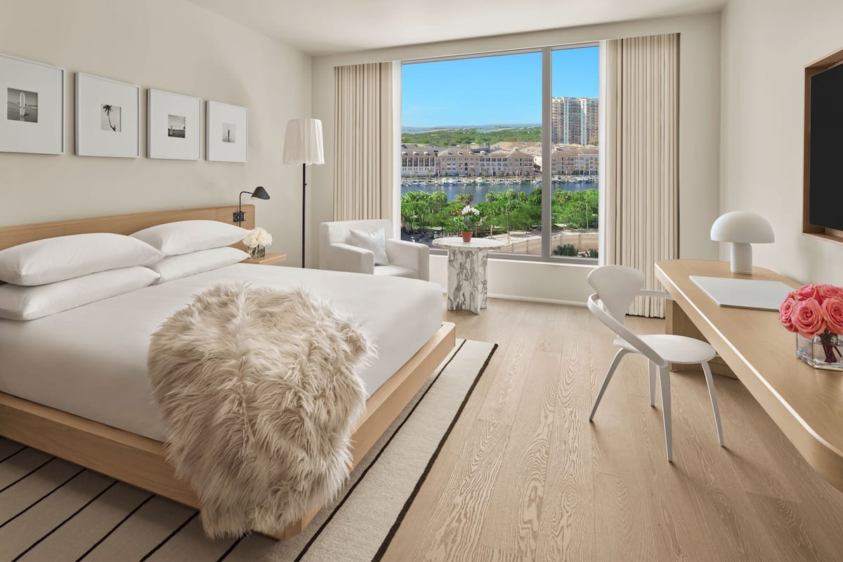 A modern hotel room with a large bed, a desk, and a view of a marina.