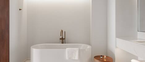 A modern bathroom with a freestanding bathtub, a wooden side table, and a white sink.