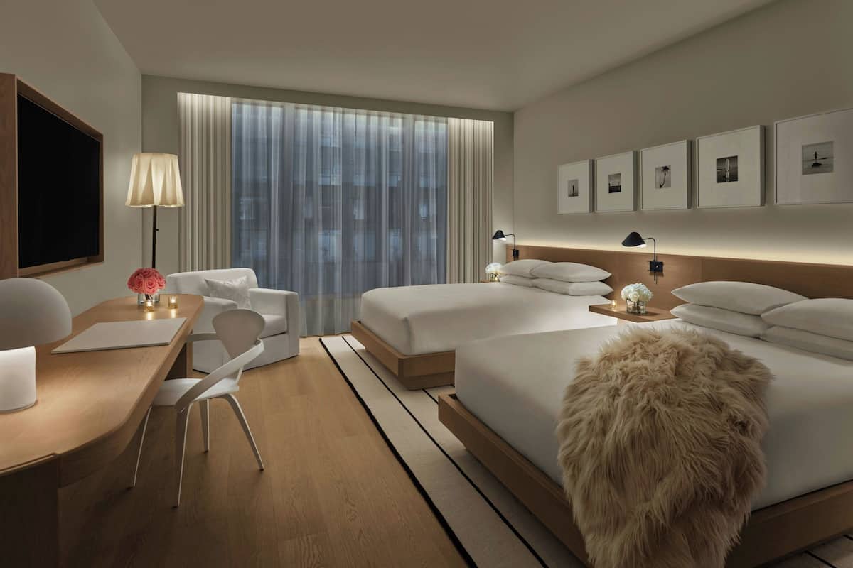 A modern hotel room with a large bed, a desk with a chair, a TV, and a window with curtains.