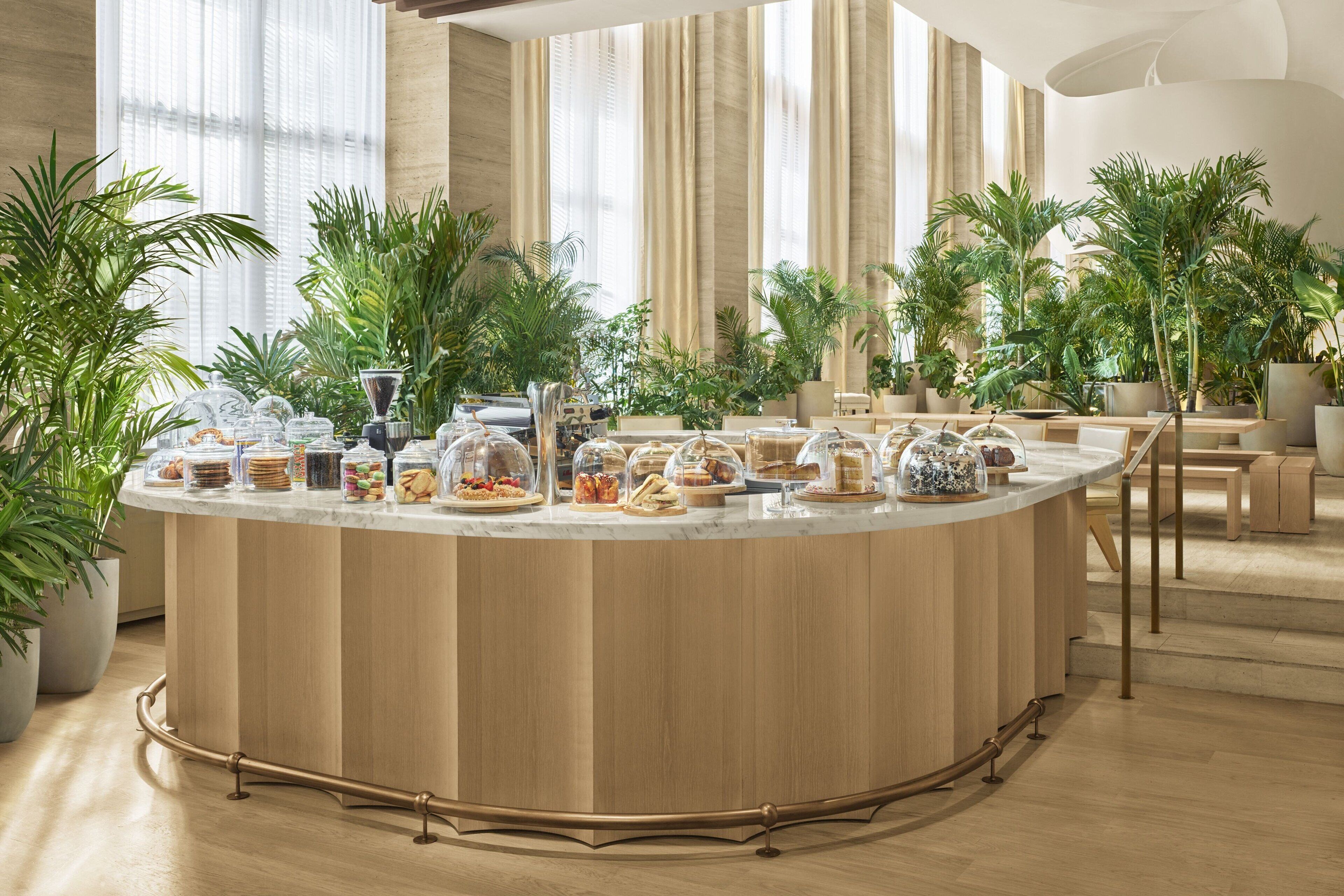 A modern breakfast bar with a marble countertop, surrounded by potted plants and featuring a variety of breakfast items.