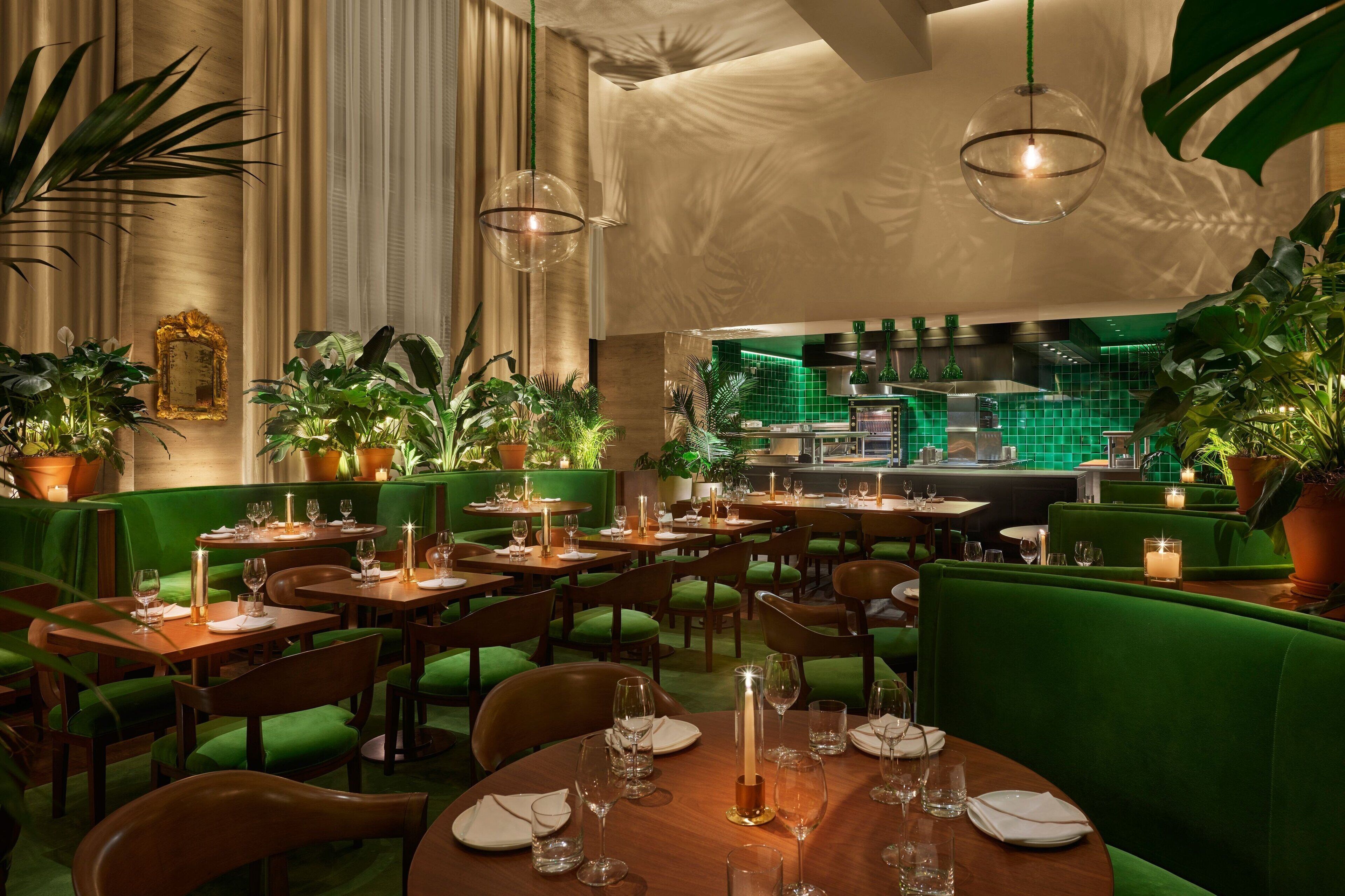 Un restaurante con asientos tapizados en verde, mesas de madera y plantas en macetas.