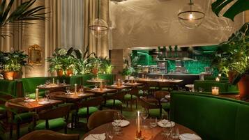 Un restaurante con asientos tapizados en verde, mesas de madera y plantas en macetas.